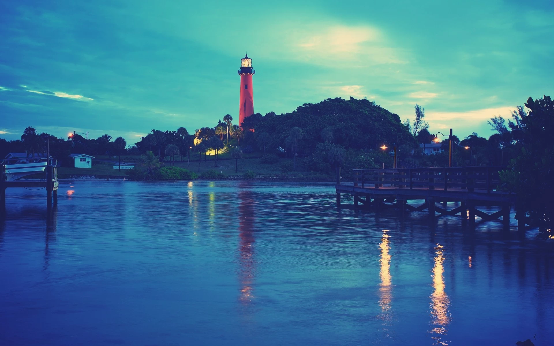A bold charcoal drawing of a tall lighthouse on a tree-covered hill at dusk, viewed across calm water with a wooden dock.